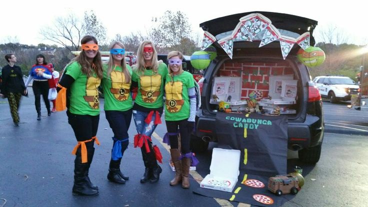 three women in green shirts standing next to a car with decorations on the trunk and back