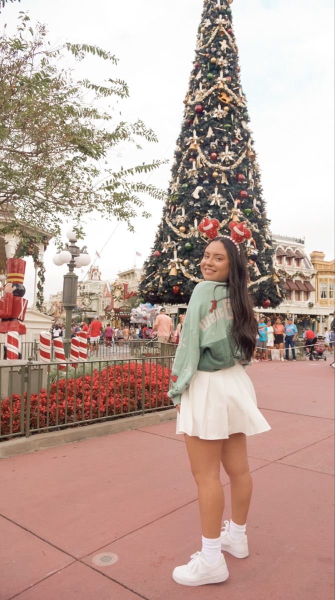 a woman standing in front of a christmas tree at the disneyland world resort, with her hands on her hips