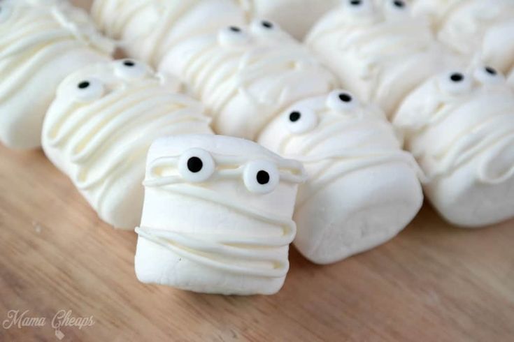 white marshmallows with googly eyes are on a wooden surface, ready to be eaten