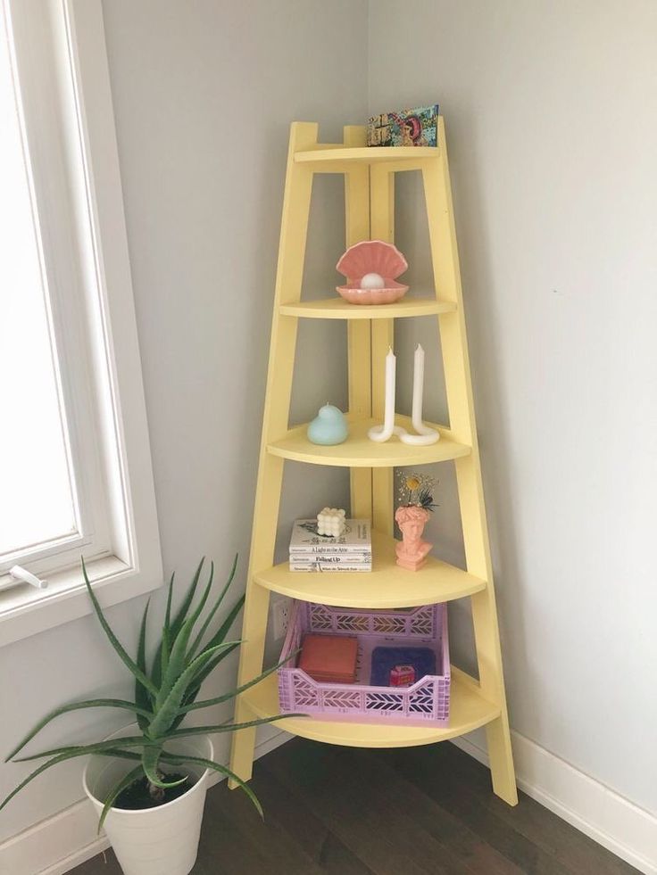 a yellow shelf next to a potted plant in a room with white walls and wooden floors