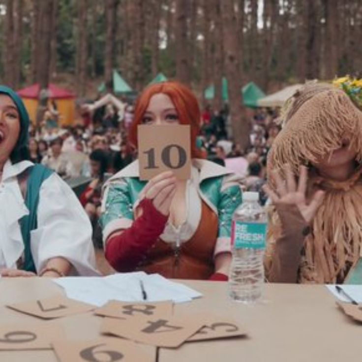 two women dressed in costumes sitting at a table with paper cutouts reading 10 on it