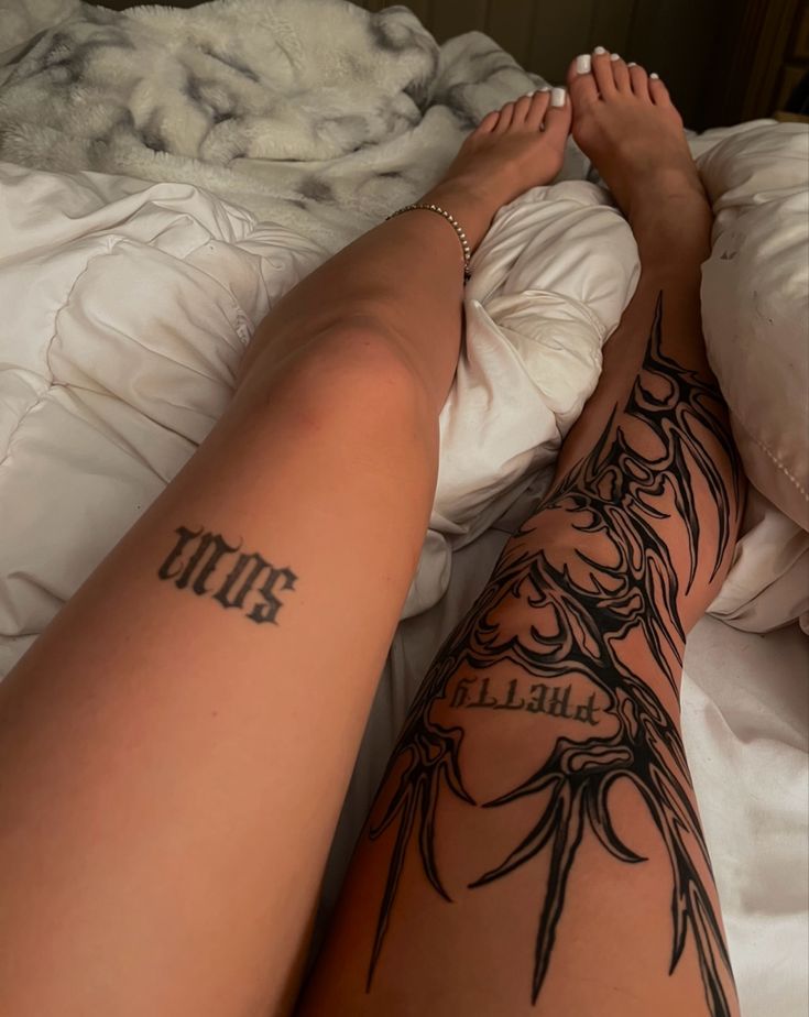 a woman laying on top of a bed next to a white comforter with tattoos on her legs