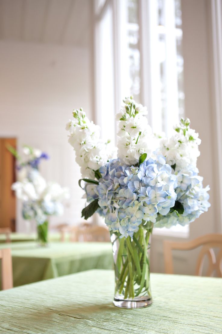 a vase filled with blue and white flowers sitting on top of a green table cloth