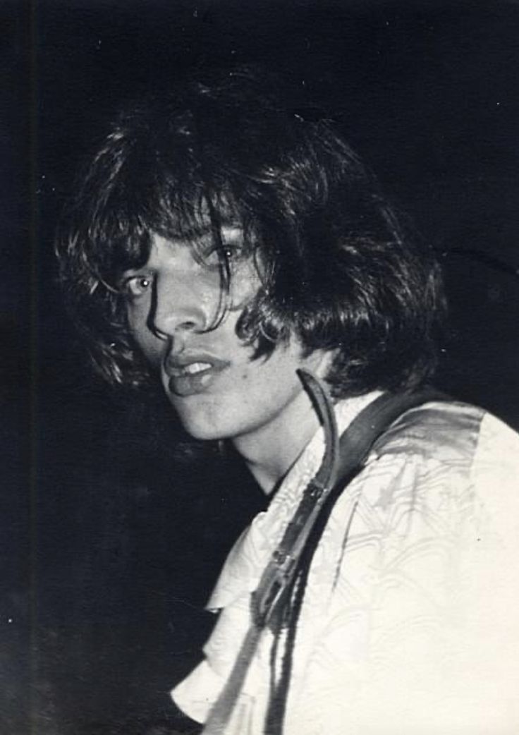 black and white photograph of a young man with long hair holding a guitar in his right hand