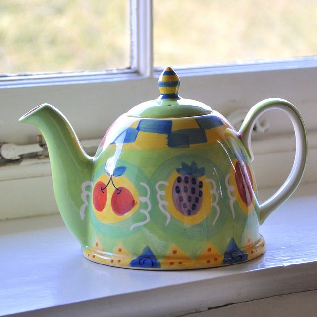 a teapot sitting on a window sill with fruit painted on the front and sides