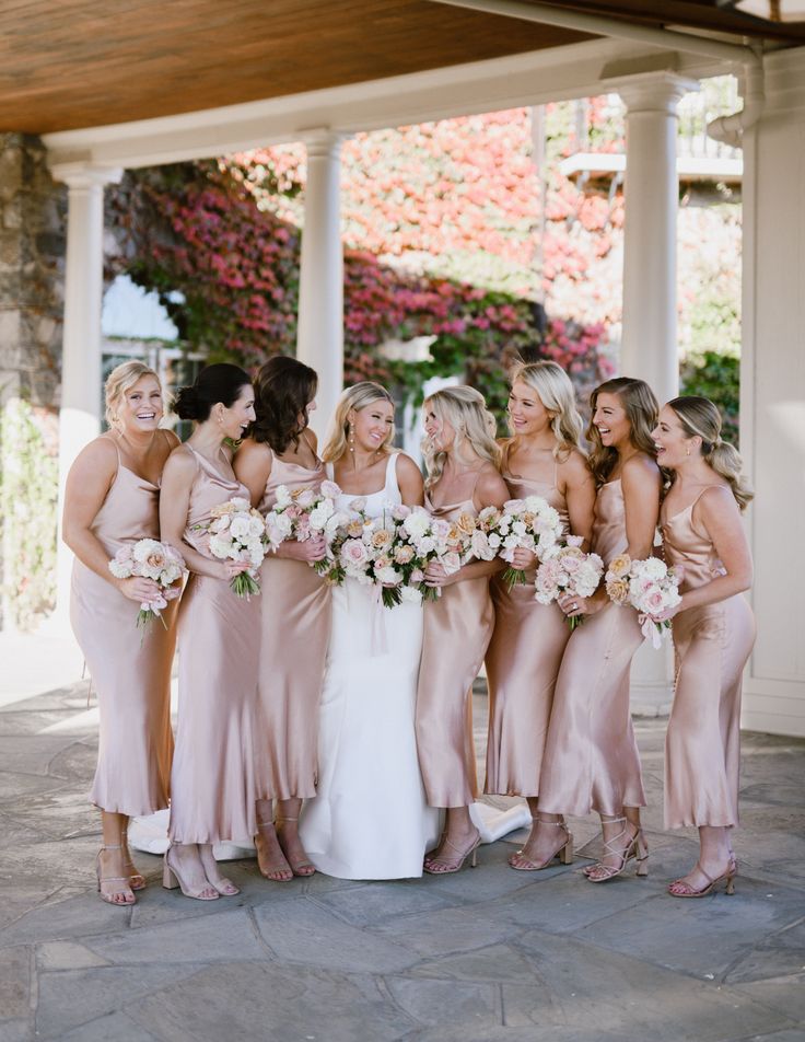 a group of women standing next to each other in front of a building holding bouquets