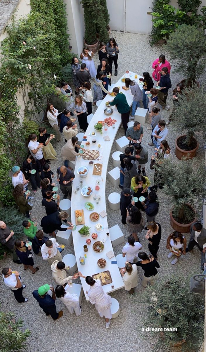 a group of people standing around a long table with food on it in an outdoor courtyard