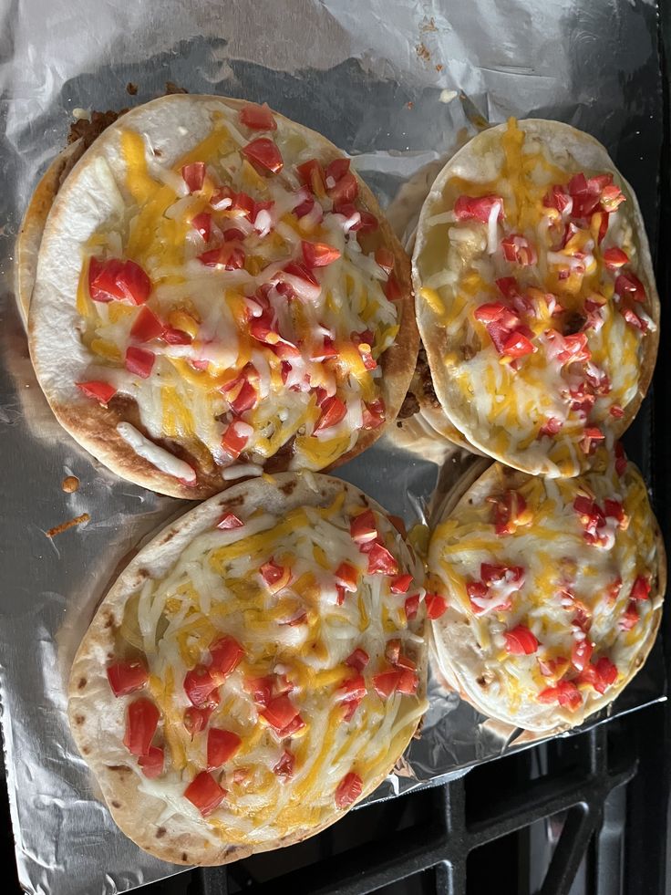 four tortillas covered in cheese and toppings sitting on top of aluminum foil