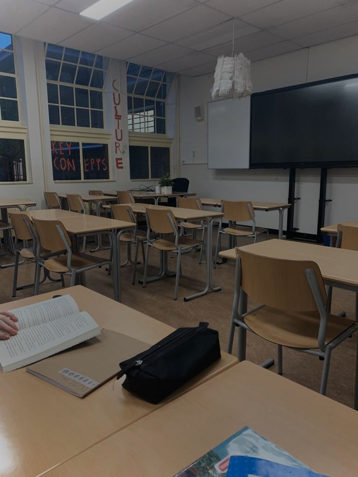 an empty classroom with desks and chairs in front of a projector screen on the wall