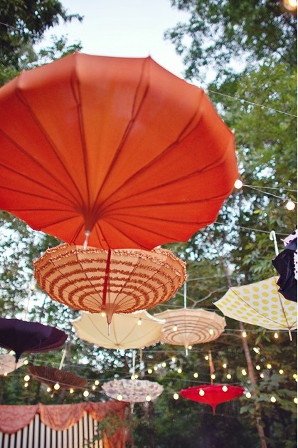 an assortment of umbrellas hanging from strings in the air with lights strung above them