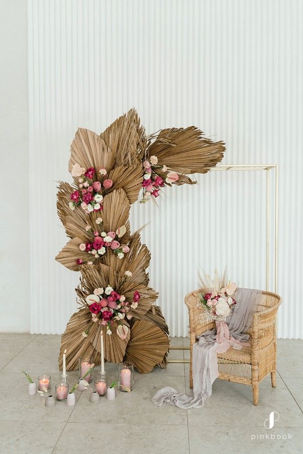 an arrangement of flowers and candles on the floor next to a wicker chair in front of a white wall