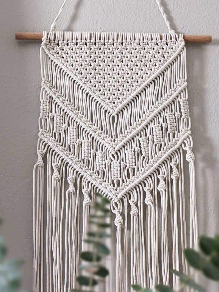 a white macrame hanging on a wall next to a potted green plant