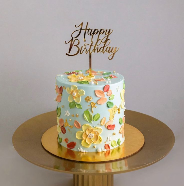 a birthday cake decorated with flowers and the words happy birthday on top is sitting on a gold plate