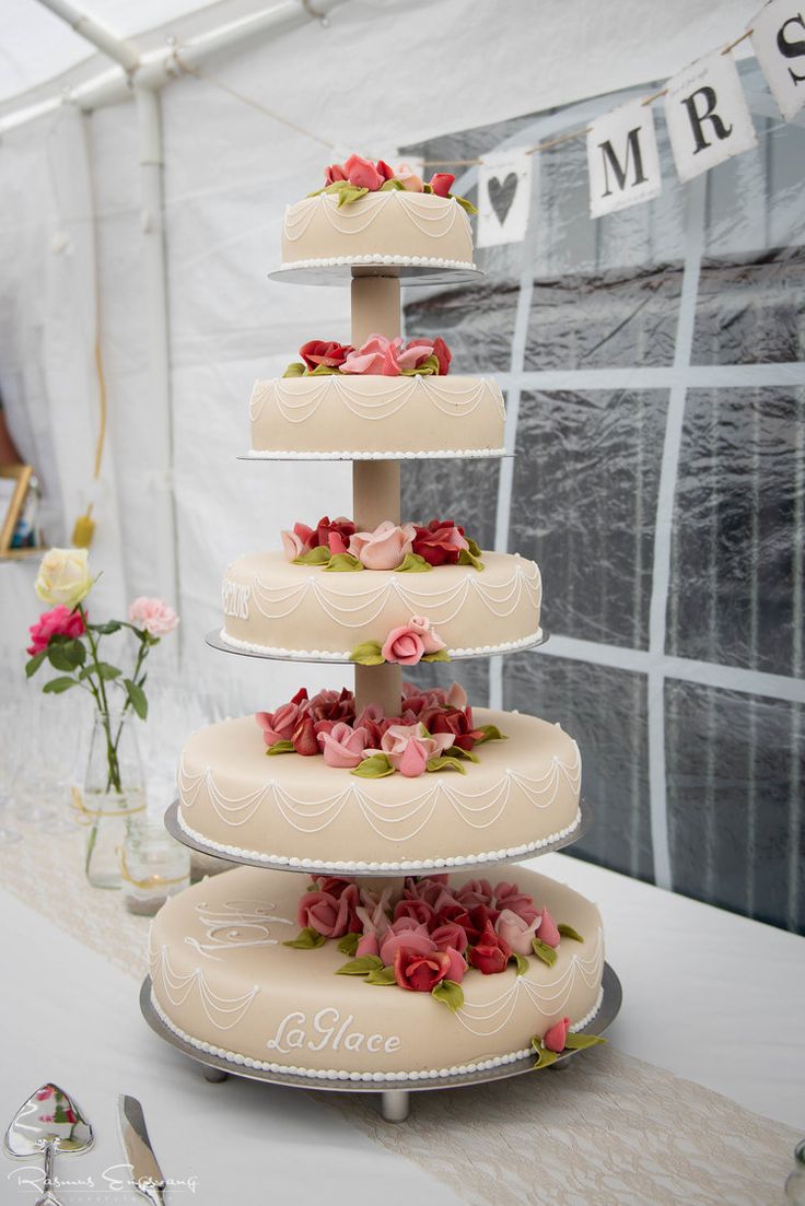 three tiered wedding cake with pink flowers on the top and bottom, in front of a white tent