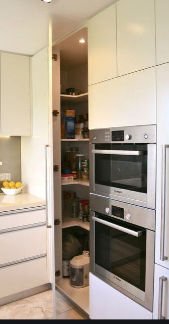 a kitchen with white cabinets and stainless steel ovens in the center, along with an open pantry