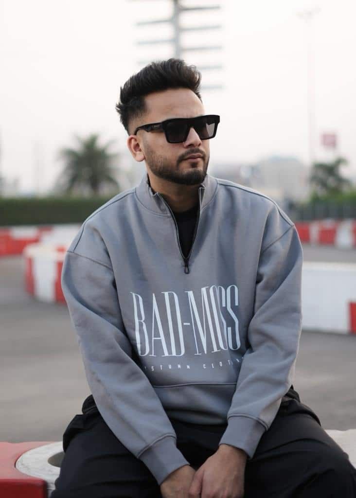 a man sitting on top of a red bench wearing sunglasses and a grey sweatshirt with bad miss written on it