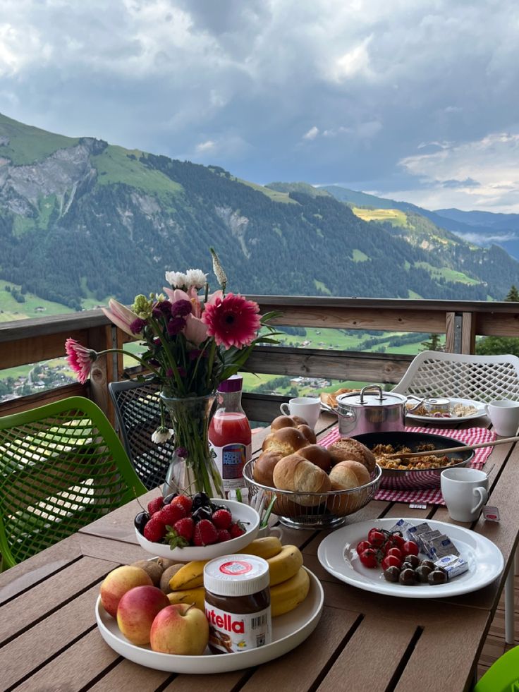 a table topped with plates of food and fruit on top of a wooden table next to a mountain