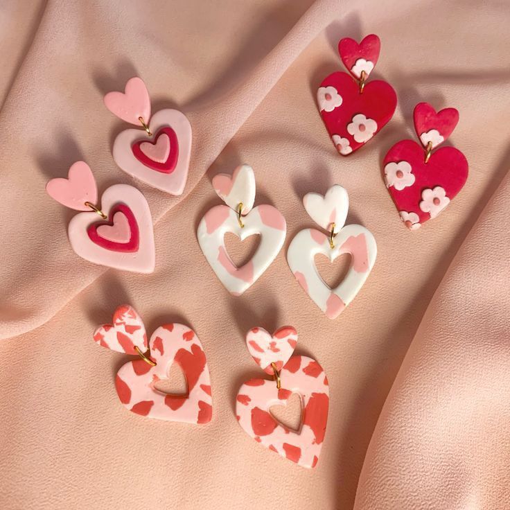 several heart shaped earrings laying on top of a pink cloth covered bed sheet with white and red hearts