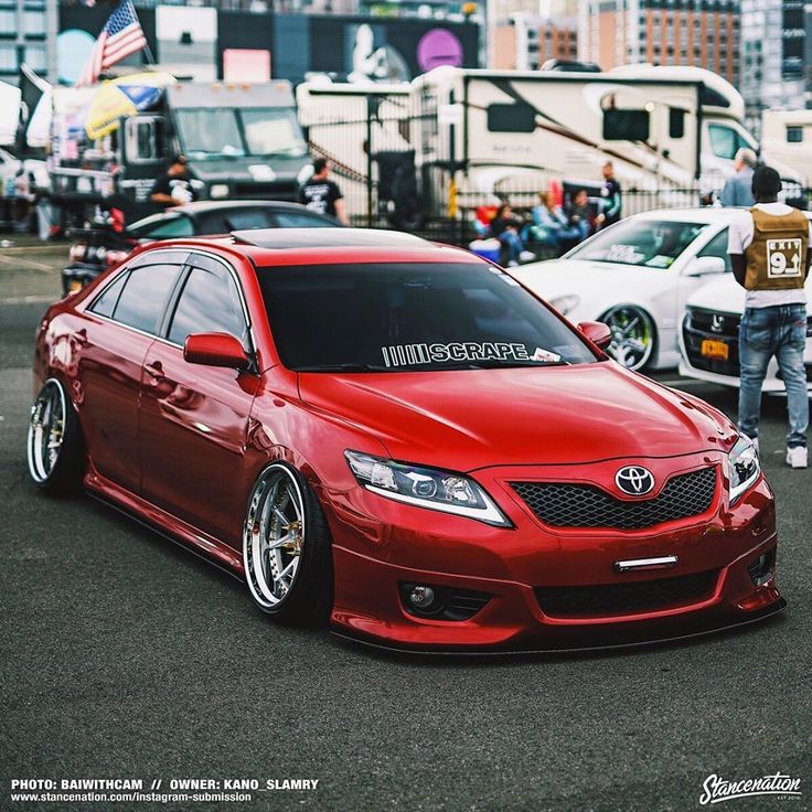 a red car is parked in the parking lot with other cars and people around it