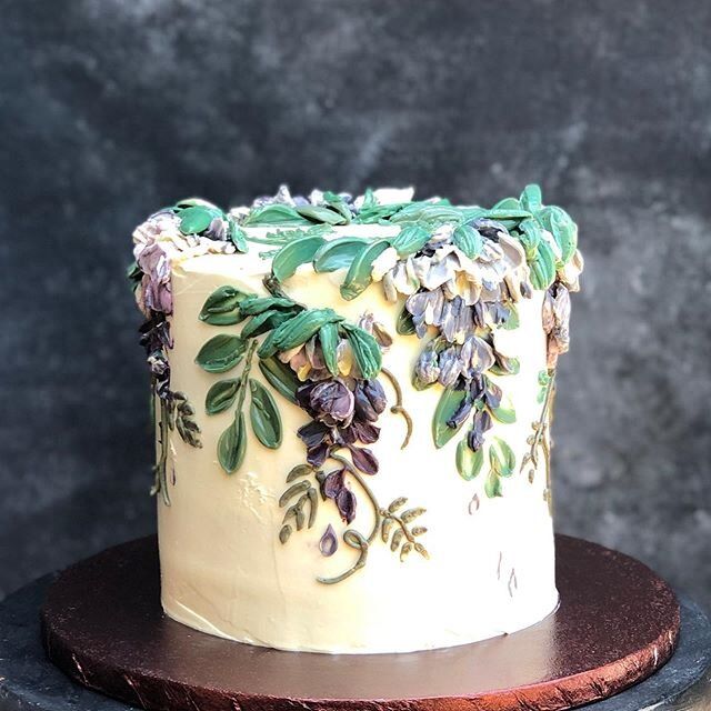 a cake with white frosting and green leaves on it sitting on a wooden stand