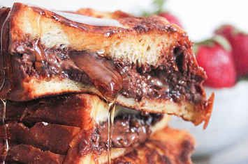 three pieces of chocolate sandwich stacked on top of each other with strawberries in the background