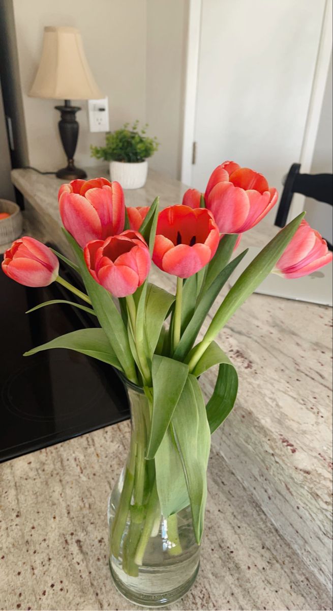 a vase filled with pink flowers on top of a counter next to a lamp and table