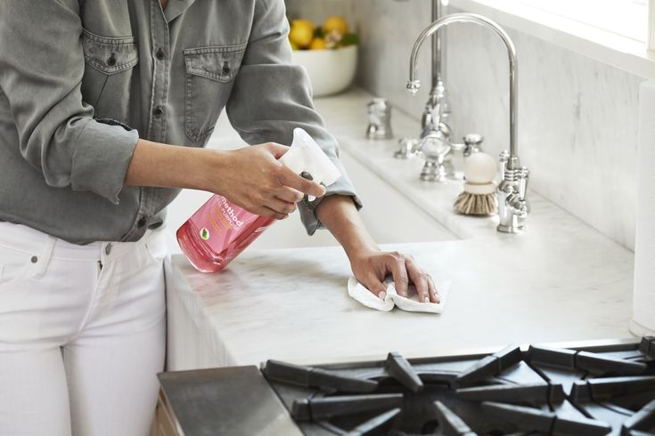 a woman is cleaning her kitchen counter with a pink hand sanitizer and cloth