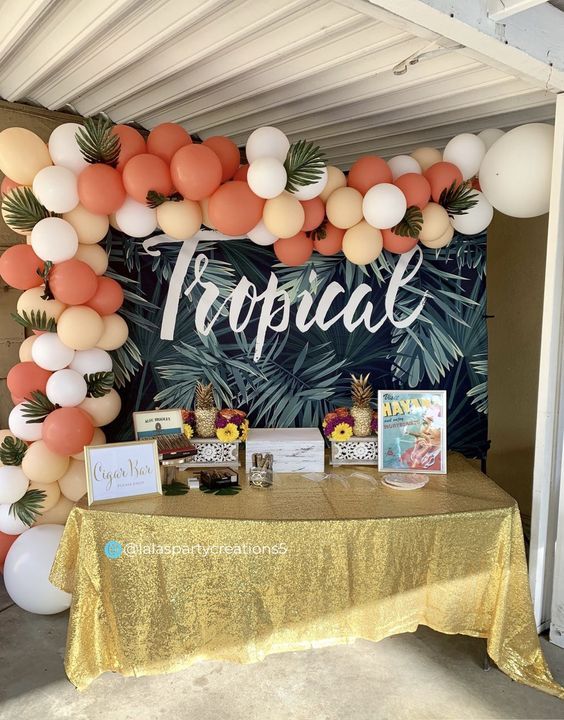 a table topped with balloons and pictures under a tropical themed sign that says tropical on it