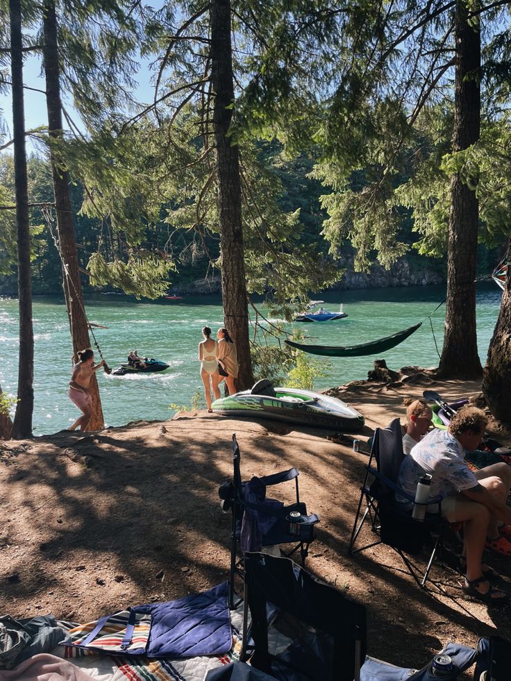 people are sitting in chairs on the shore of a lake with hammocks and canoes