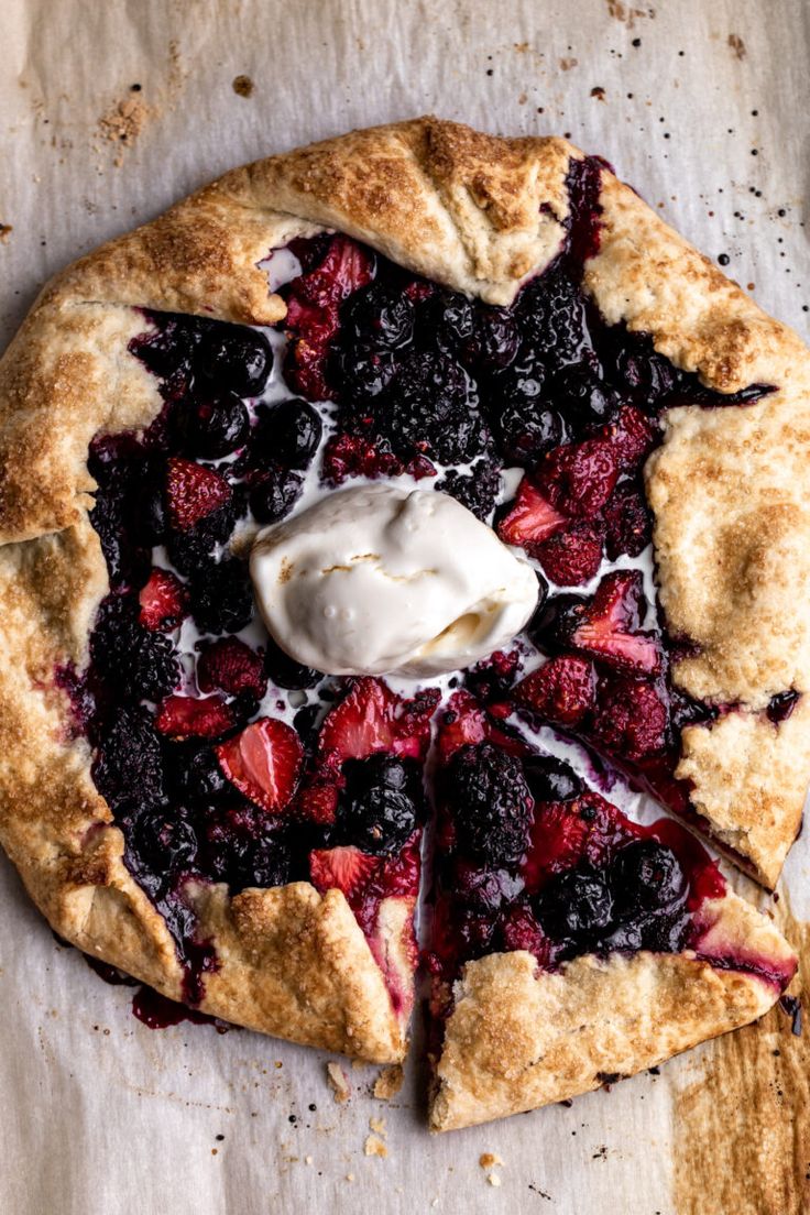 a pie topped with berries and whipped cream on top of a piece of parchment paper