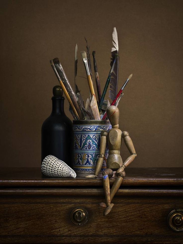 a wooden doll sitting on top of a table next to a vase filled with paint