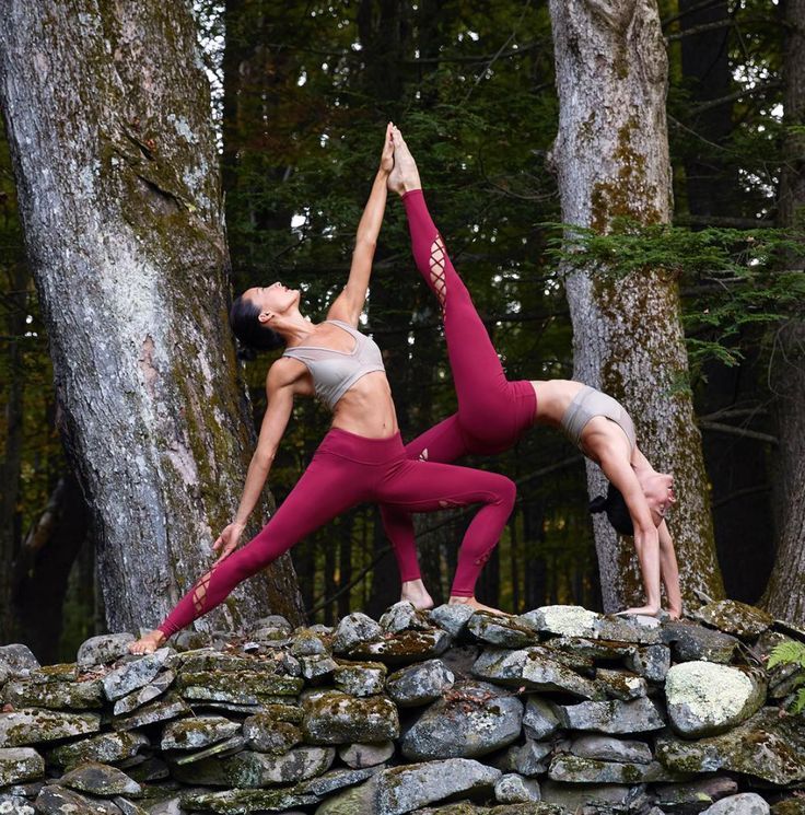 two women are doing yoga in front of some trees and rocks with their hands together