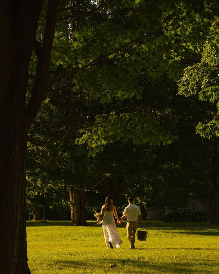 a man and woman walking through a park holding hands