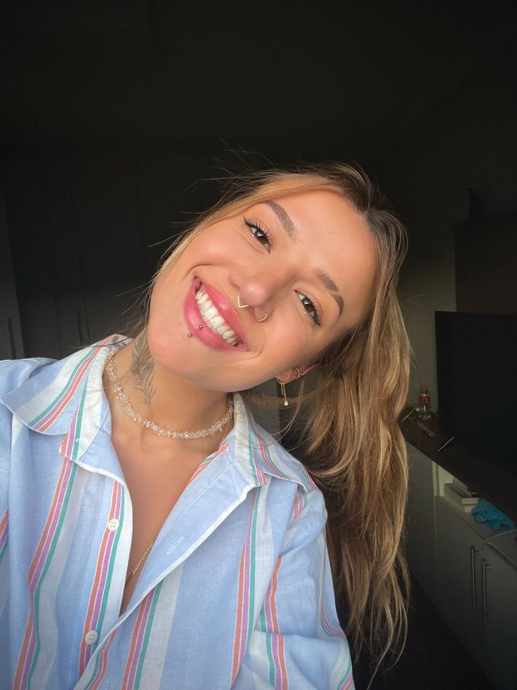 a woman smiling and wearing a blue shirt with multicolored stripes on the collar