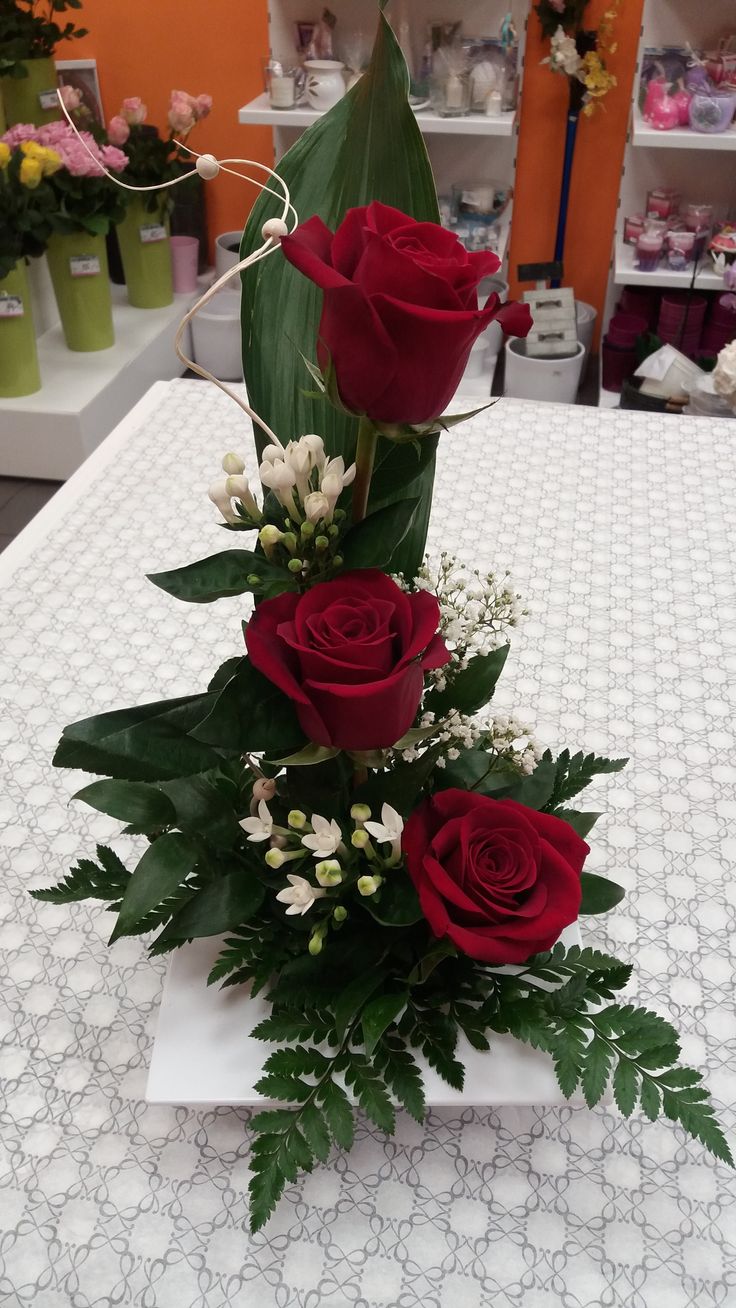 three red roses and greenery on a table in a flower shop with other flowers