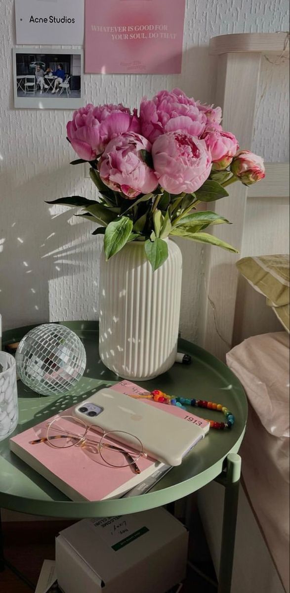 pink flowers are in a white vase on a green table with other items around it