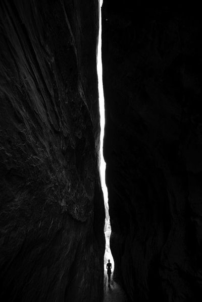 a person standing in the middle of a narrow tunnel with light coming from behind it