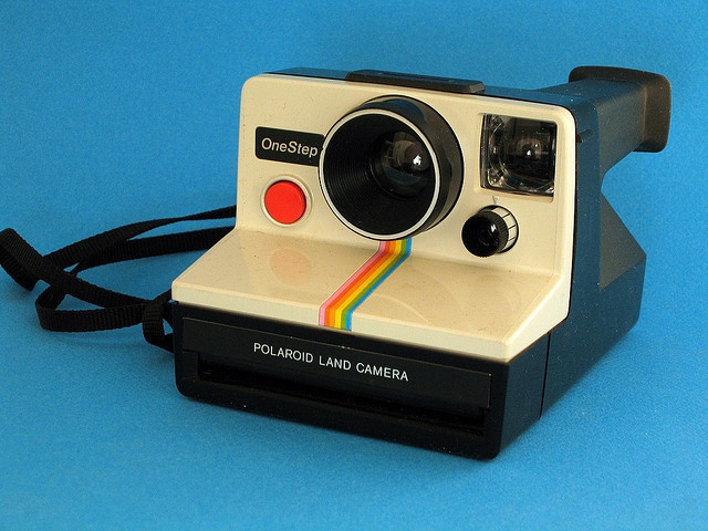 an old polaroid camera sitting on top of a blue surface with a black strap