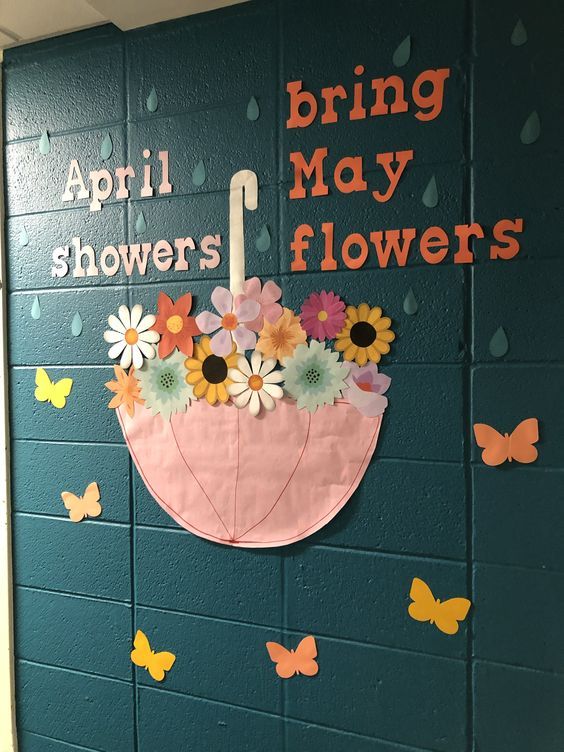 a bulletin board with flowers and an umbrella in the center on a school hallway wall