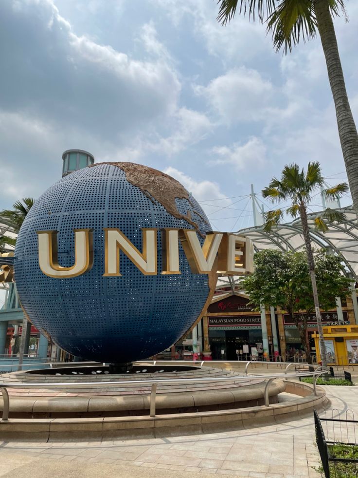 a large blue globe with the word universal on it in front of a building and palm trees