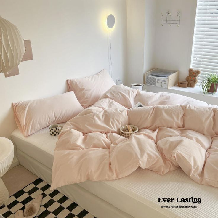 an unmade bed with pink sheets and pillows in a white room next to a black and white checkered floor