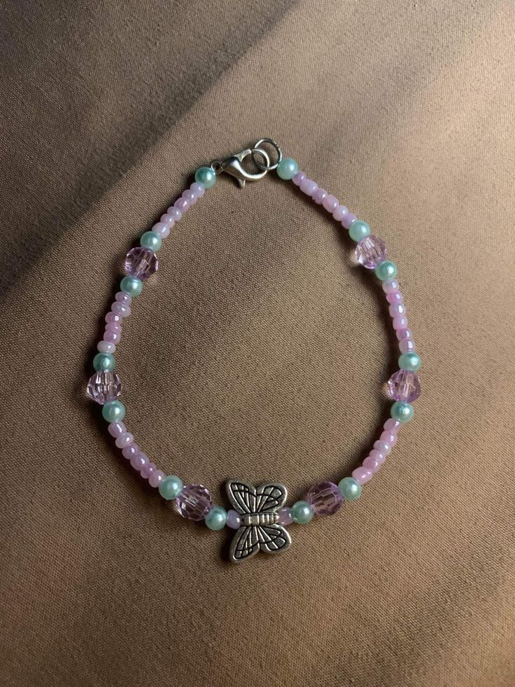 a bracelet with beads and a butterfly charm on the clasp, sitting on a brown surface