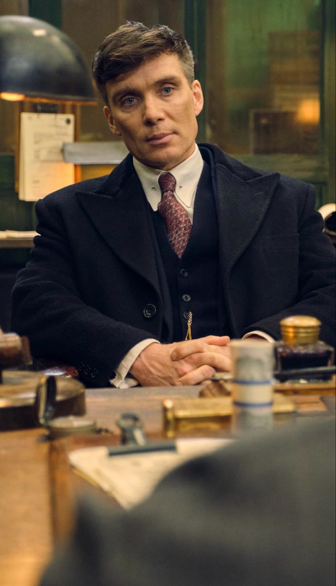 a man sitting at a desk with his hands folded in front of him, wearing a suit and tie