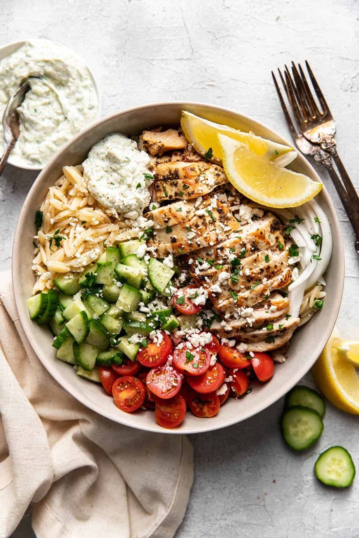 a white bowl filled with chicken, cucumber and tomato salad next to some lemon wedges