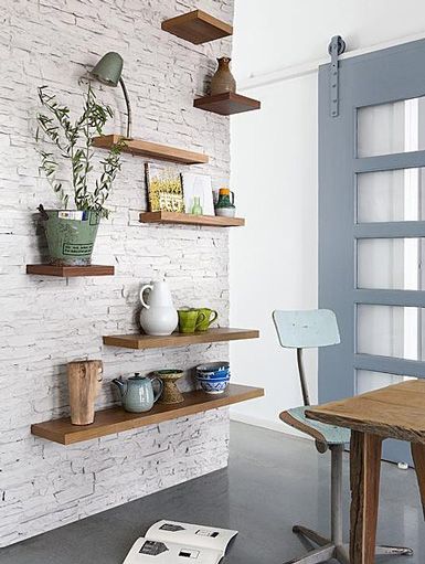 a table and some shelves with plants on them in front of a white brick wall