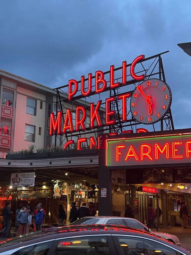 a car is parked in front of a building with a large neon sign that reads public market on farmer's