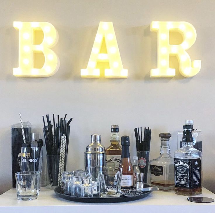 a bar with liquor bottles and glasses on the counter next to an illuminated sign that says bar