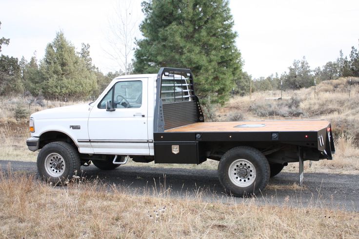 a white pickup truck parked on the side of a road next to a field and trees