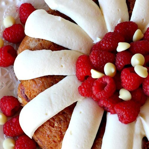 a cake with white frosting and raspberries on top is decorated in the shape of a flower