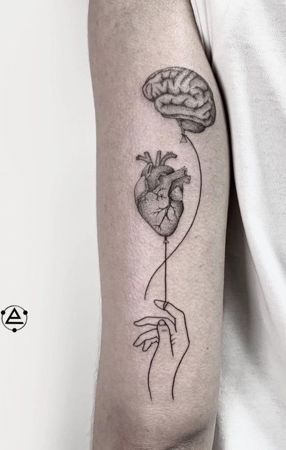 a person with a tattoo on their arm holding a heart and brain in the shape of a balloon